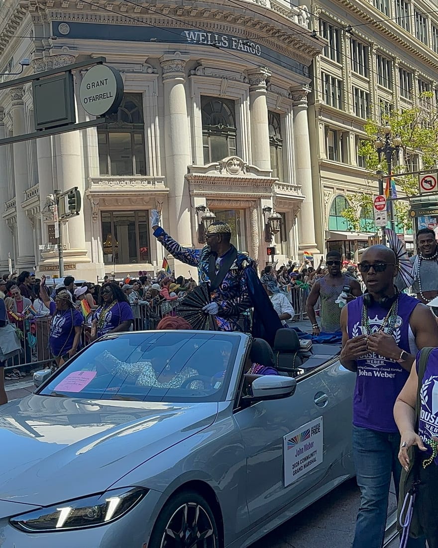 John Weber waving from a convertible on Market Street at Grant and O'Farrell during the San Francisco Pride Parade, his contingent in purple shirts
